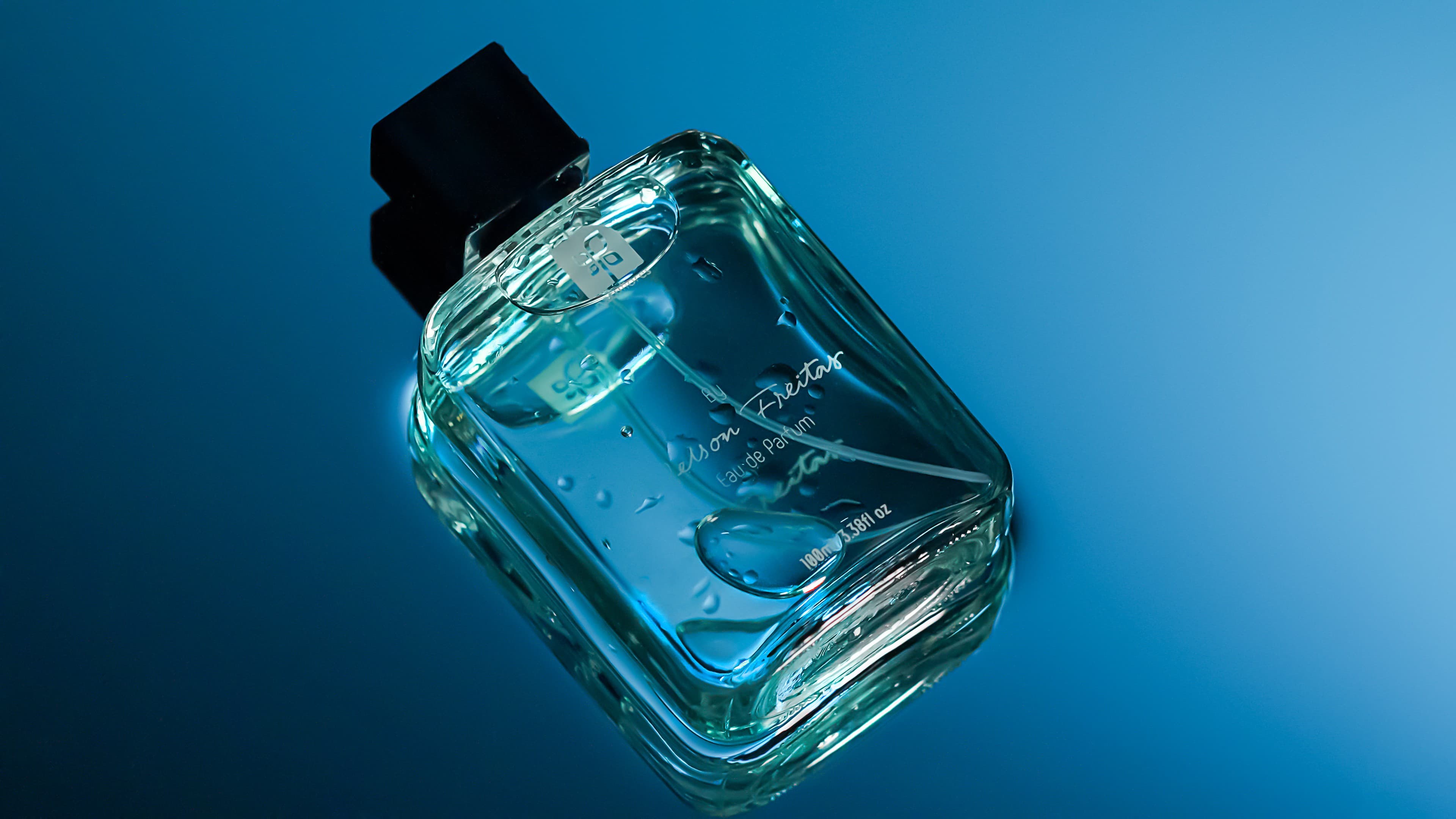 Frasco do perfume sobre fundo azul com respingos de água