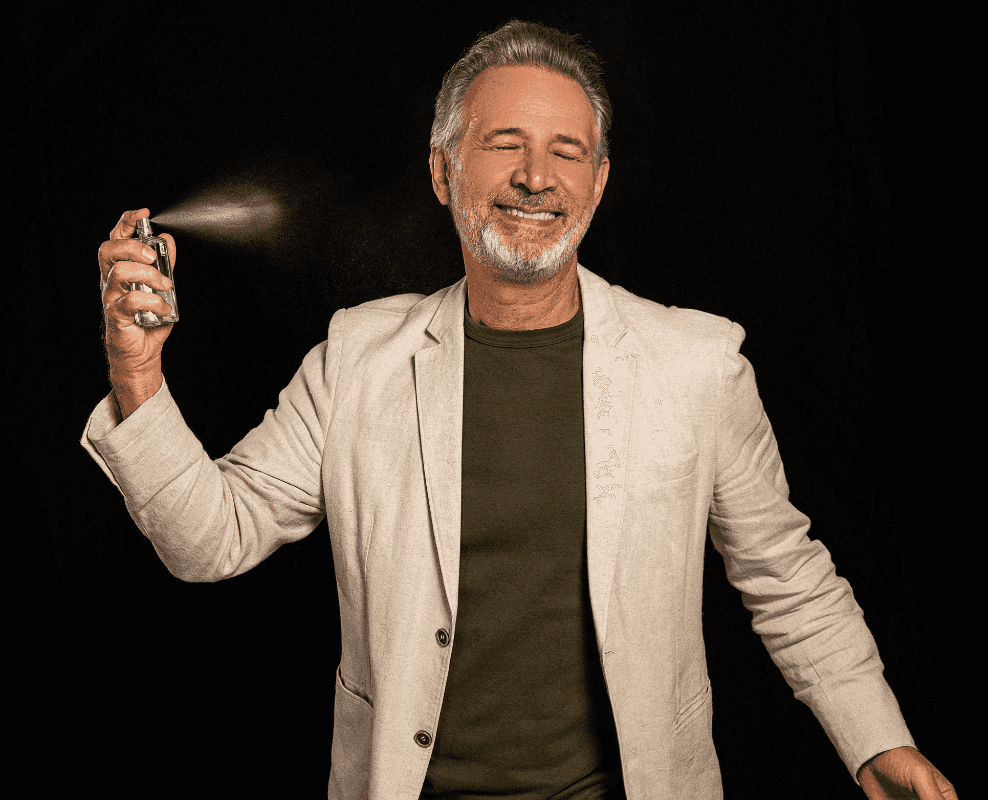 Nelson Freitas rindo enquanto borrifa o perfume, fundo preto