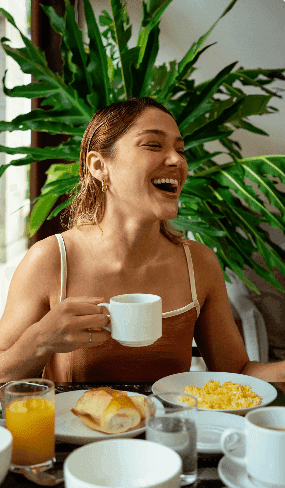 Hóspede rindo com xícara de café entre as plantas
