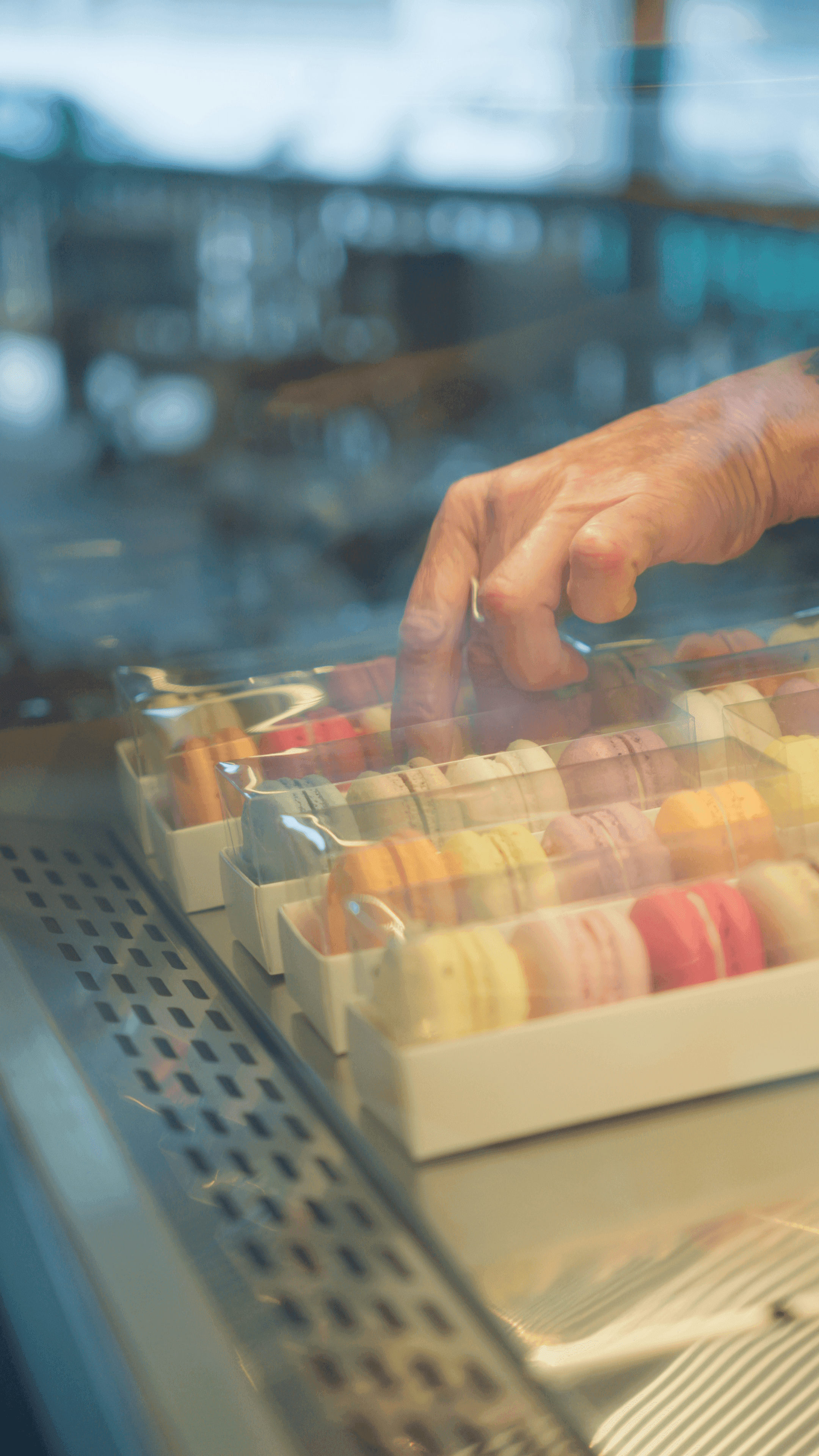Mão escolhendo macarons na bandeja da vitrine refrigerada