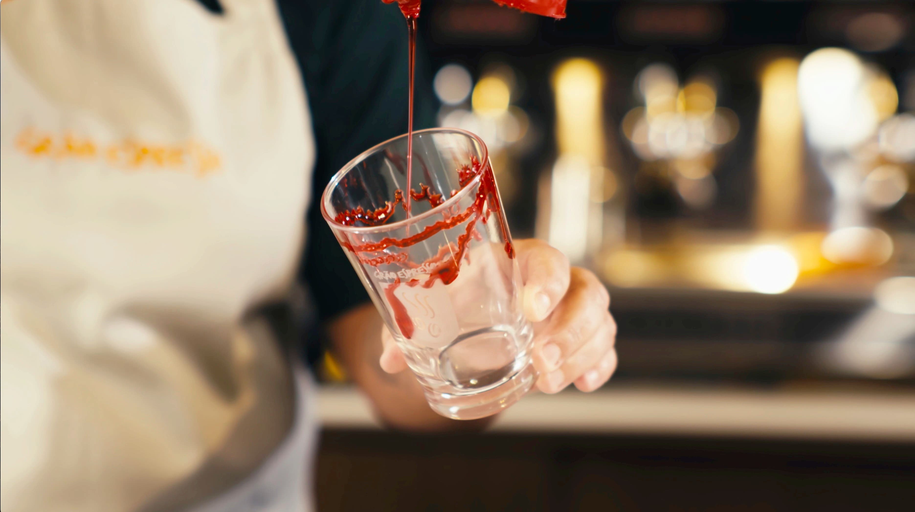 Barista servindo calda vermelha no copo atrás do balcão
