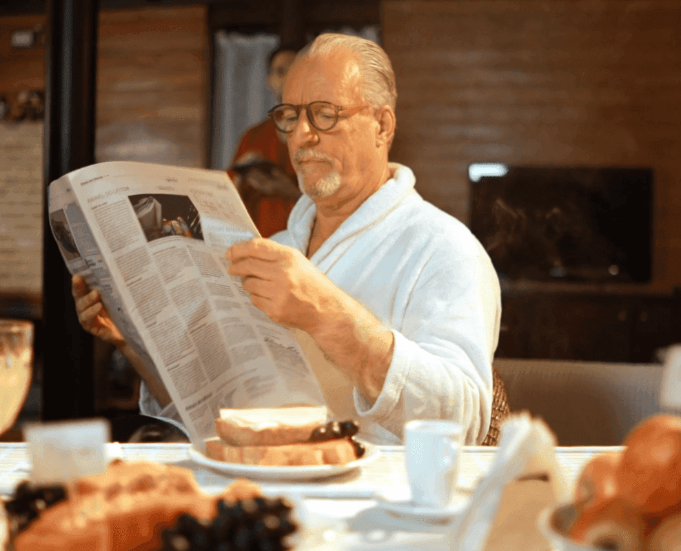 Senhor lendo jornal à mesa do café da manhã