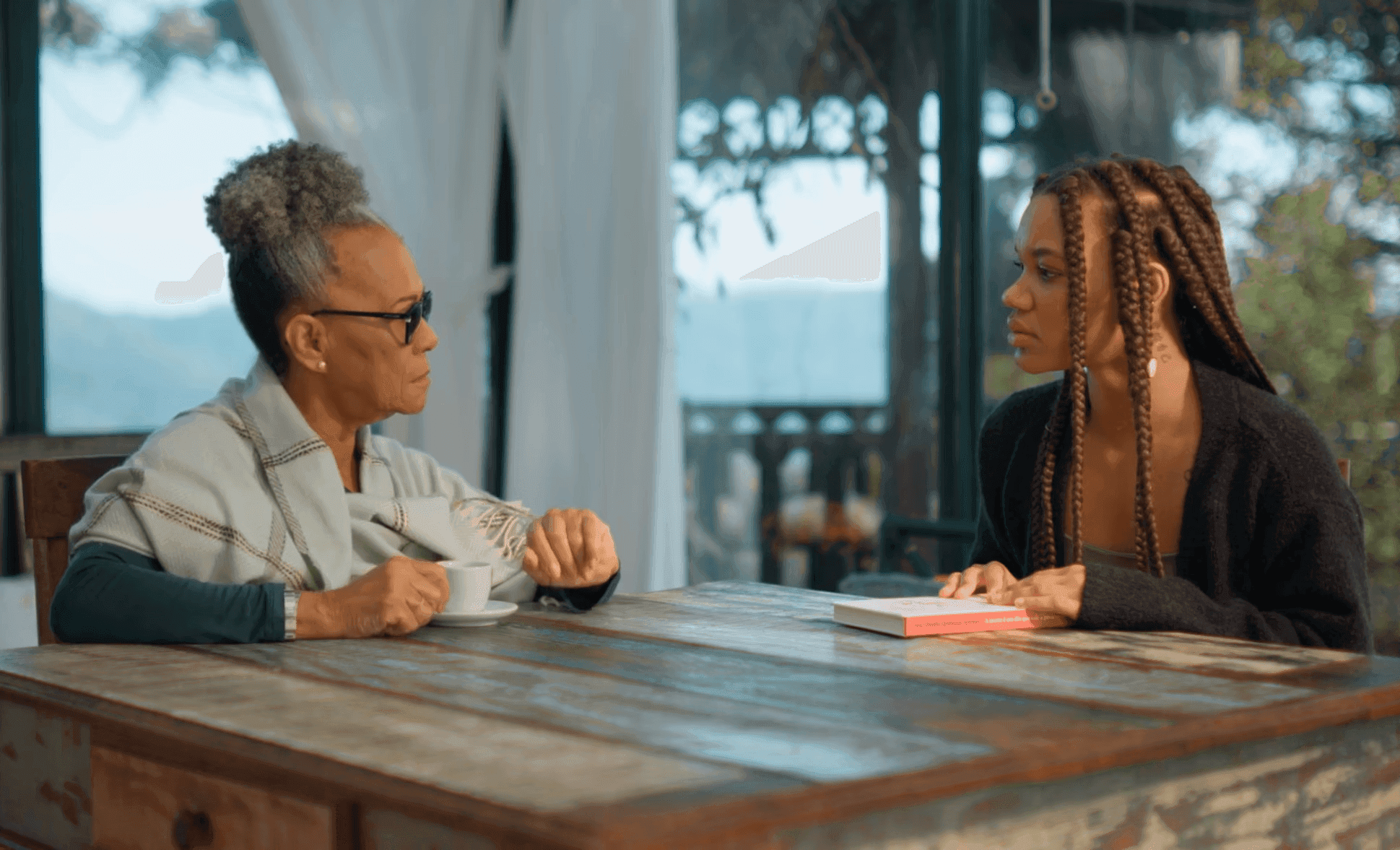 Duas mulheres conversando à mesa com vista para fora