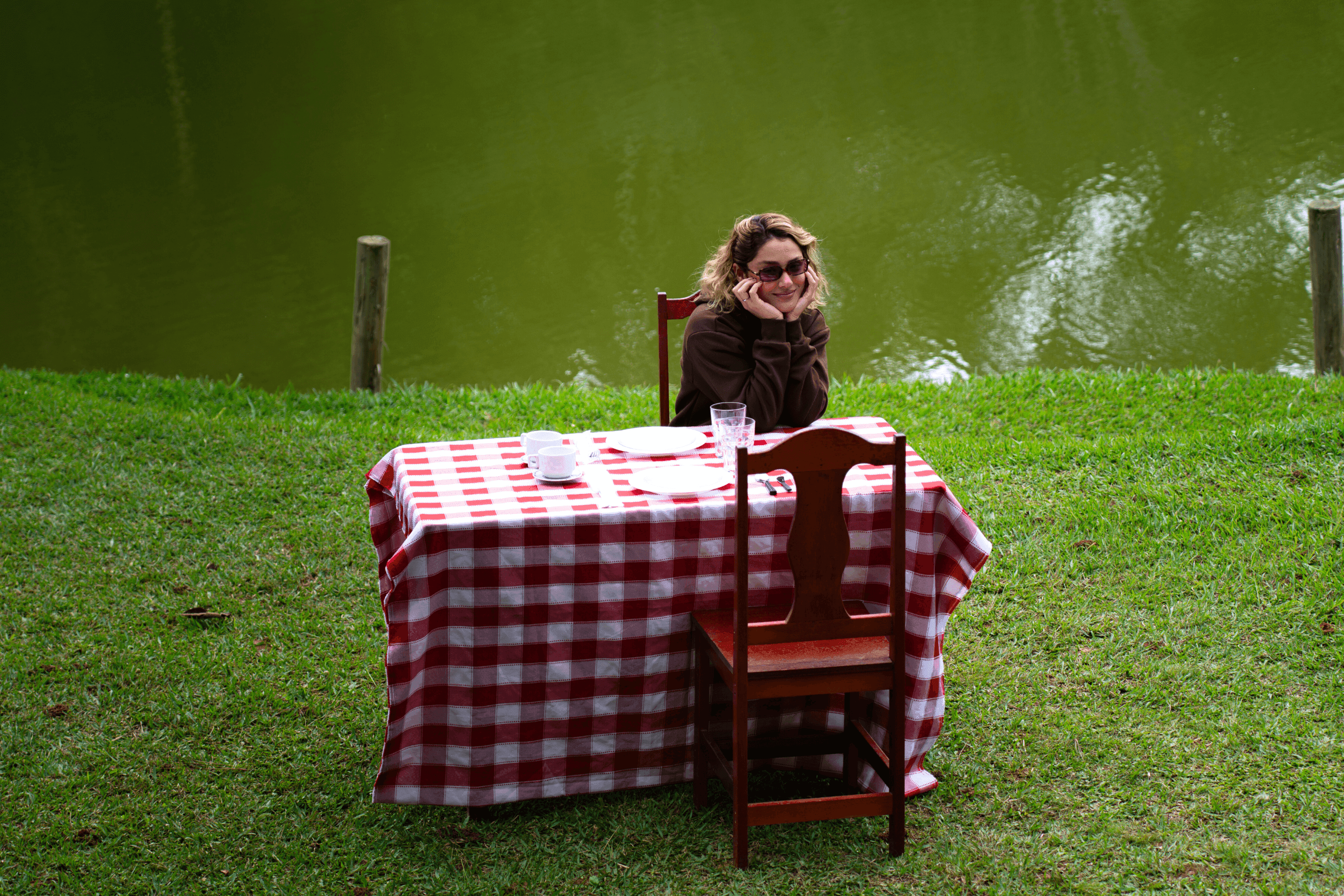 Mesa posta com toalha xadrez vermelha na grama à beira do lago